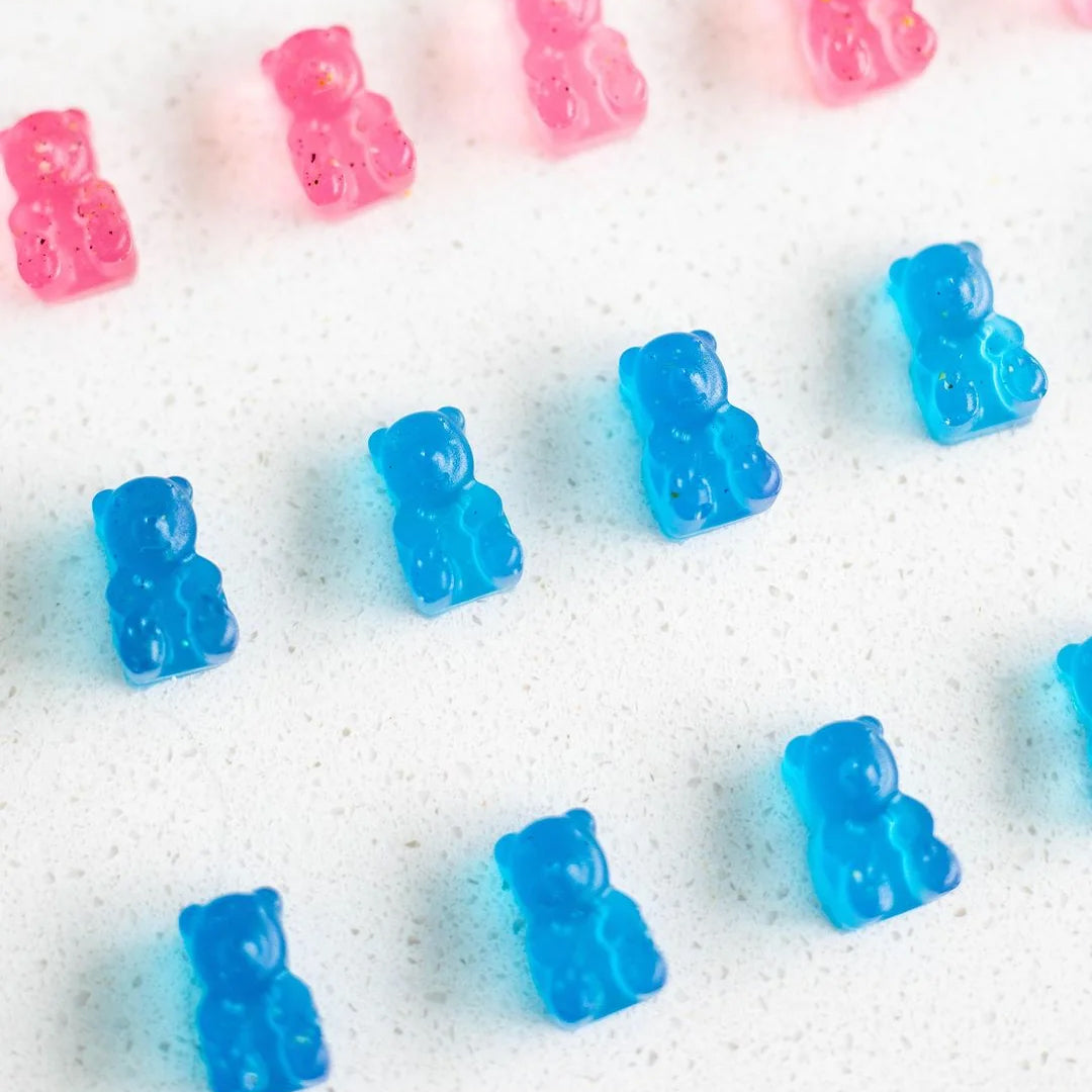 Assorted blue and pink gummy bears scattered on a speckled white surface.