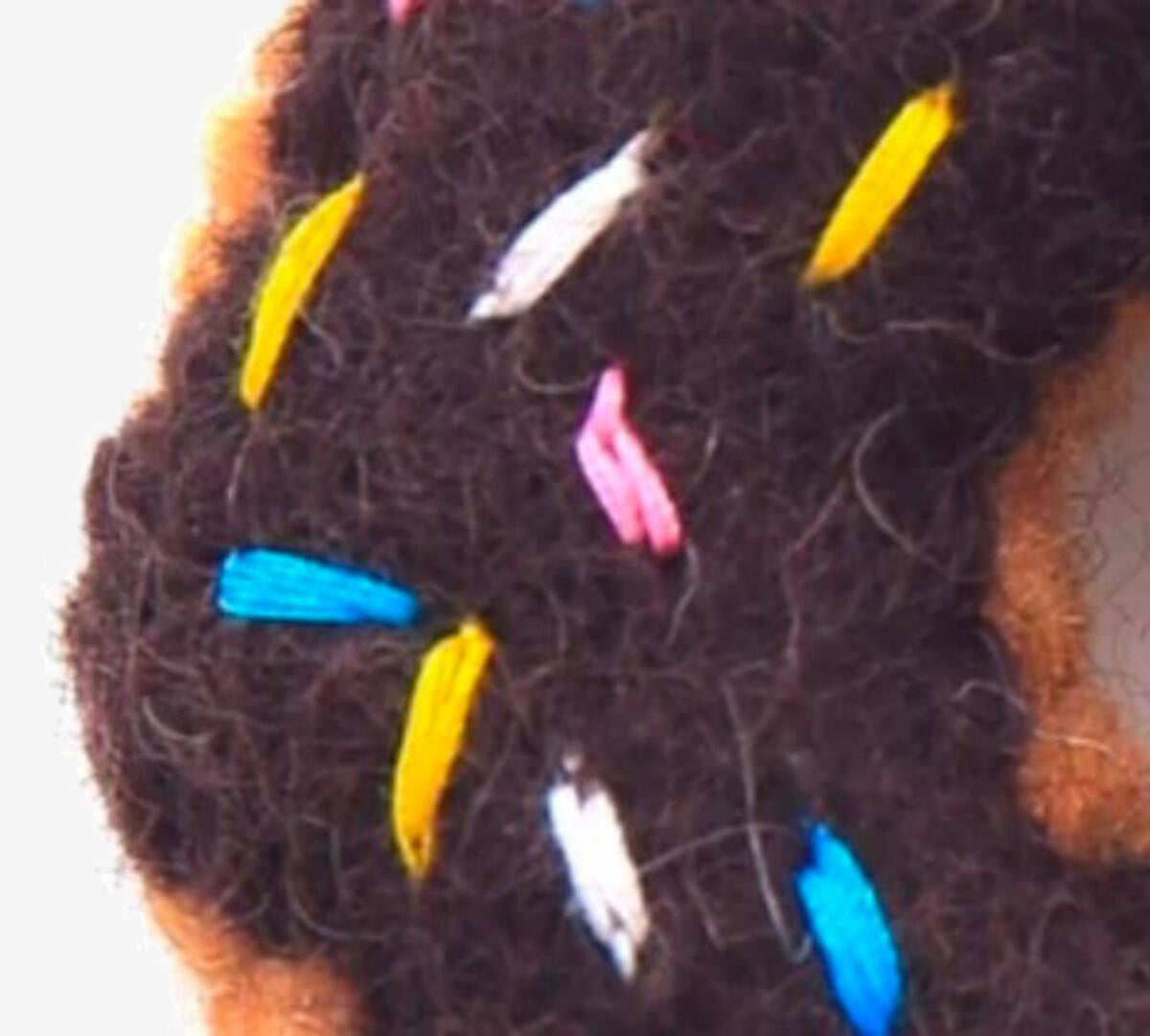 Close-up of colourful threads or entangled in dark brown chocolate coloured fabric.