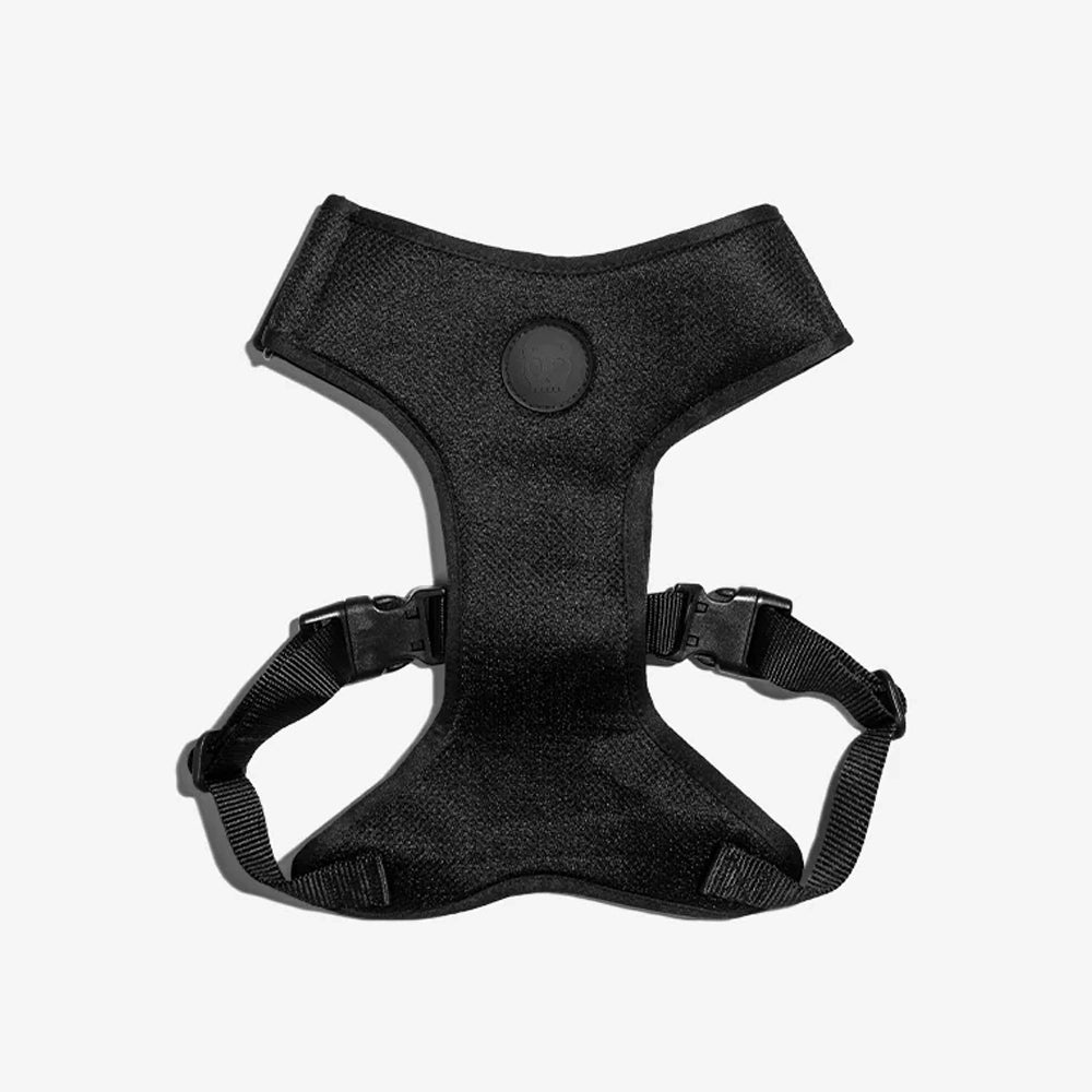 A black dog harness with adjustable straps and a round logo on the back, displaying a Y-shape design for comfort and support.