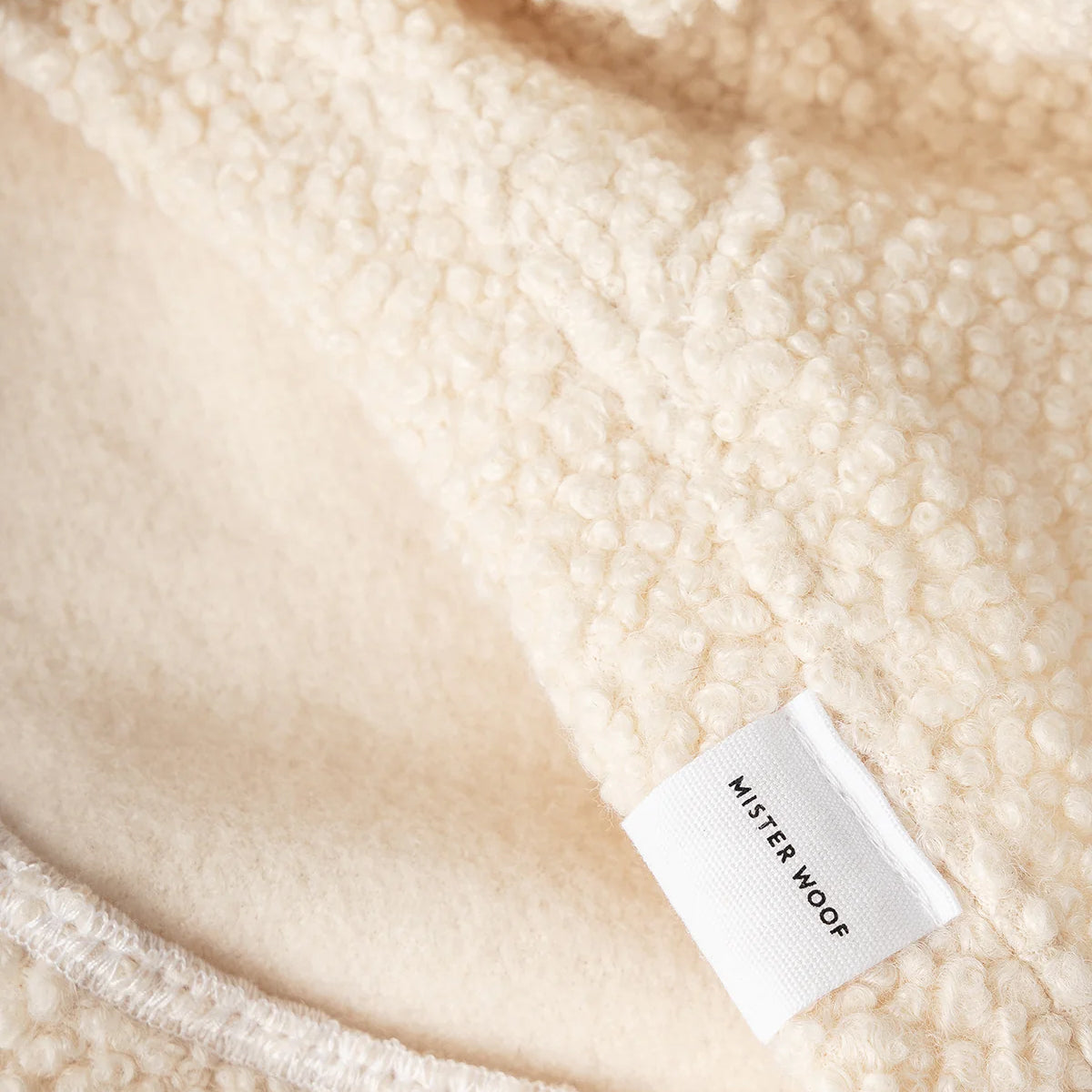 Close-up of a soft, cream-coloured fabric with a textured surface and a tag reading "Mister Woof" sewn into the edge.