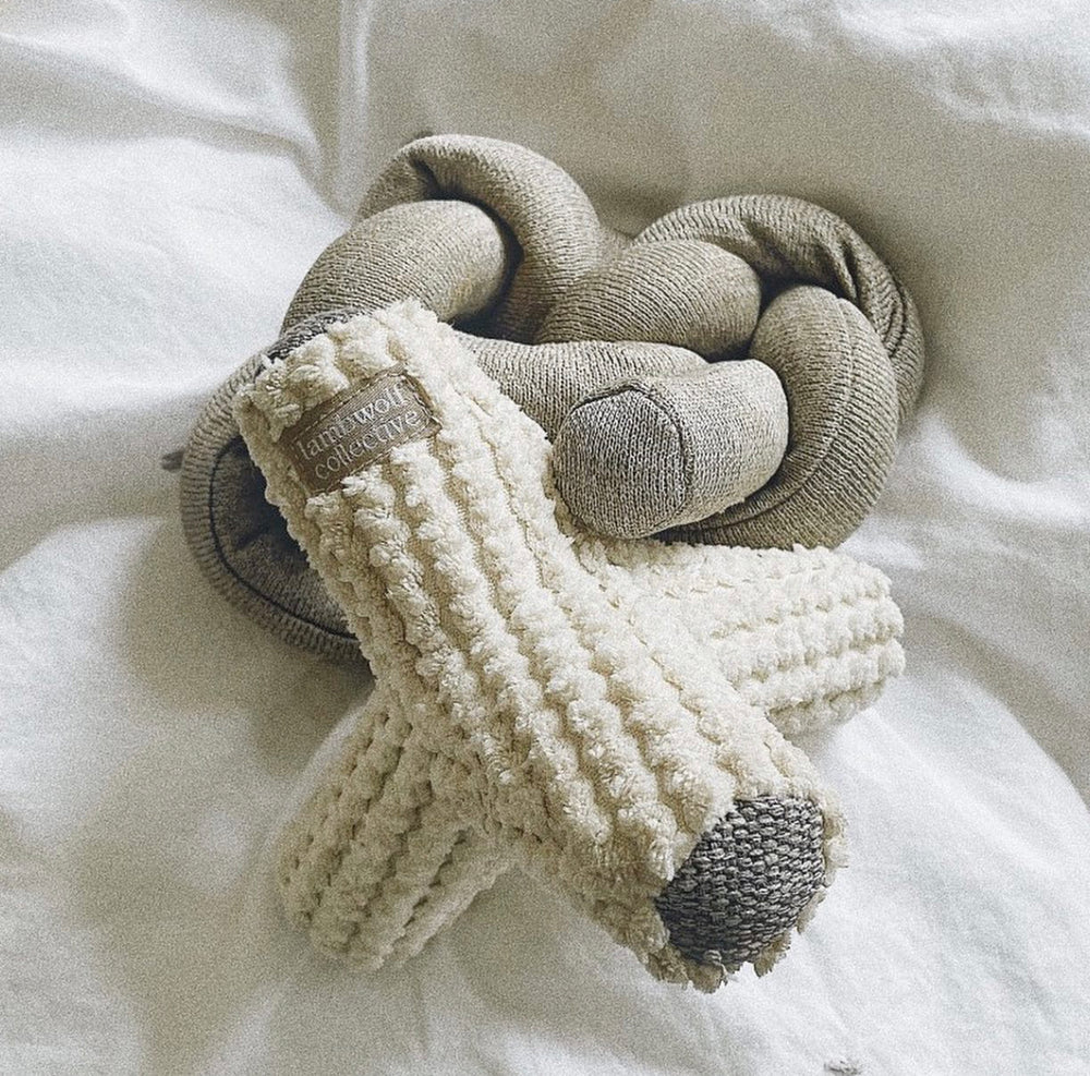 A plush, beige dog toy with a textured surface rests beside a soft, twisted grey fabric, on a light blanket background.