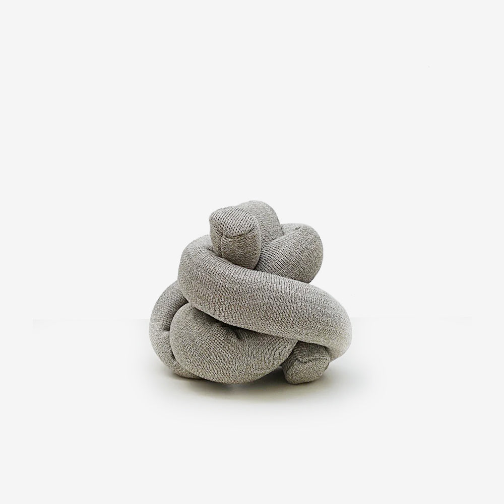 A twisted, gray textile knot sculpture, resembling a soft, abstract art piece, sits on a white background.