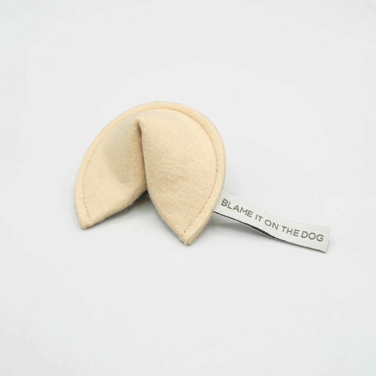 A plush fortune cookie with a tag saying "BLAME IT ON THE DOG" on a white background.