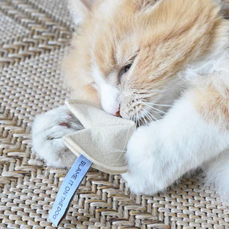 A ginger and white cat snuggling with a small cloth hat on a woven mat.