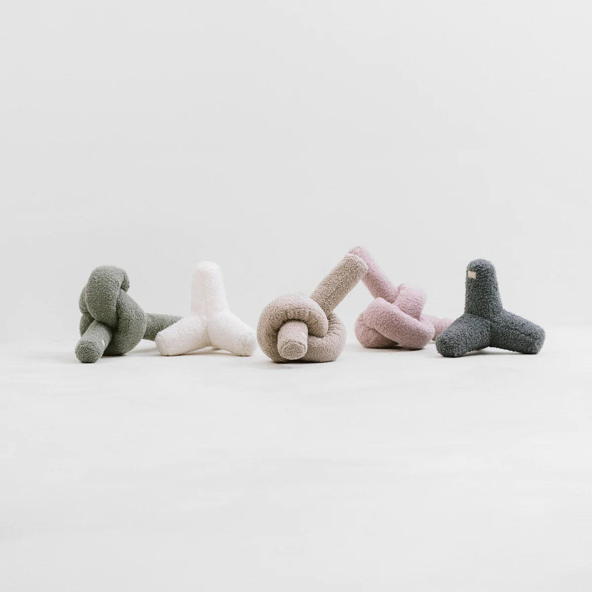 Five soft, abstract fabric sculptures in pastel colours arranged in a line against a minimalist background.
