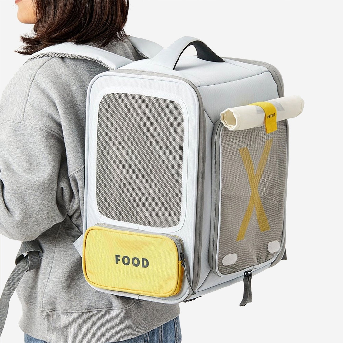 Person wearing a grey pet carrier backpack with a "FOOD" pouch and rolled-up mat.