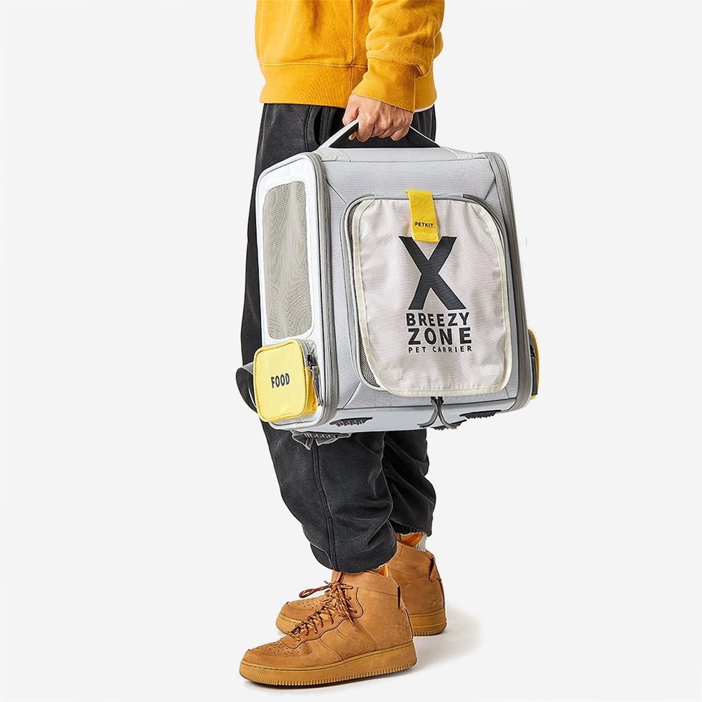 Person holding a transparent pet carrier with the label "Breezy Zone Pet Carrier".