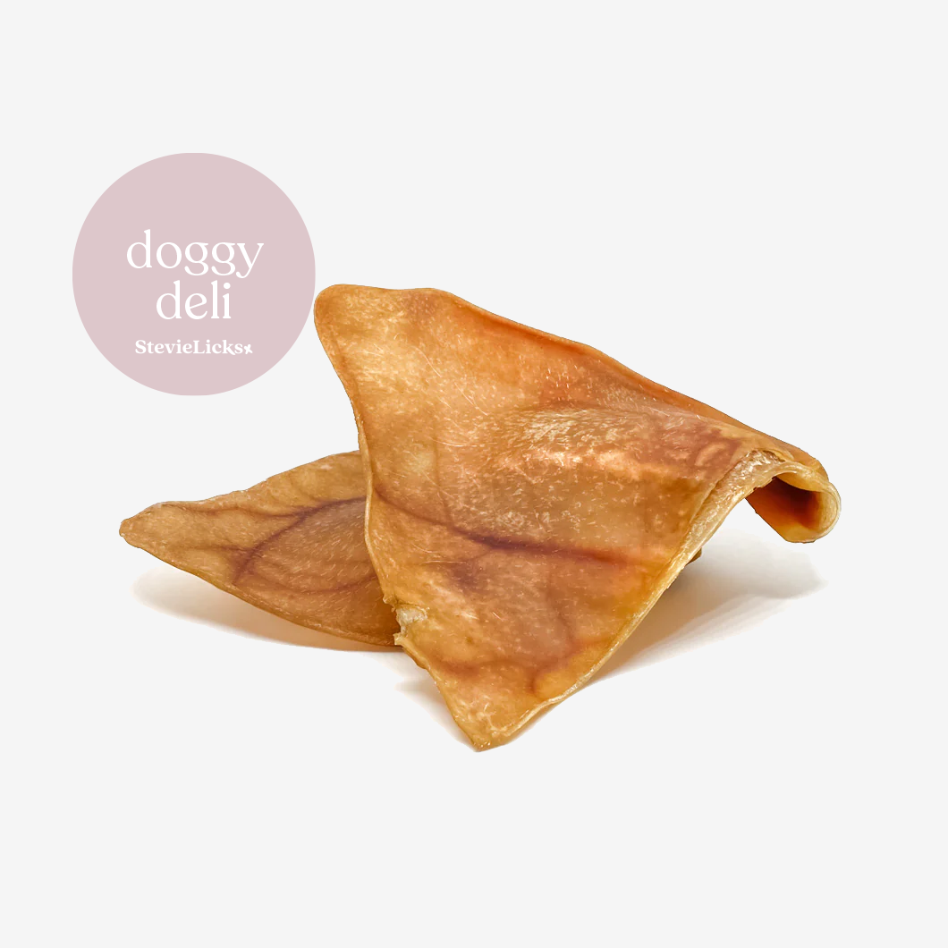 Two dog treats pig ears, with the logo "doggy deli" in a pink circle above.