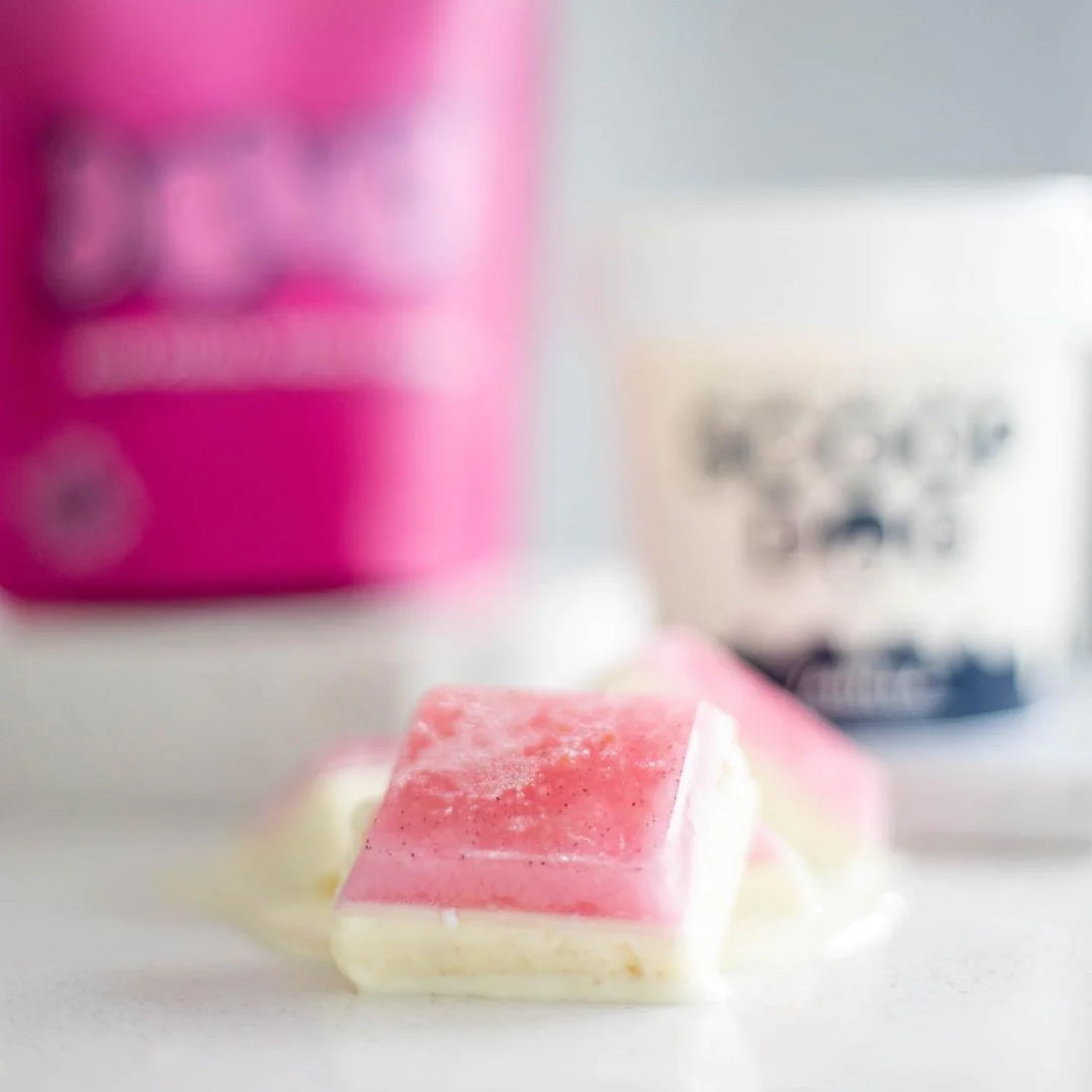 Layered strawberry and vanilla fudge squares with blurred ice cream containers in the background.