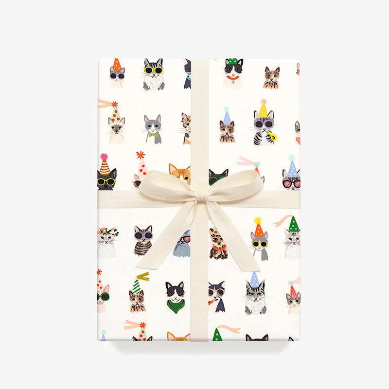 Gift-wrapped package featuring playful cat illustrations in festive attire, tied with a creamy ribbon on a light background.