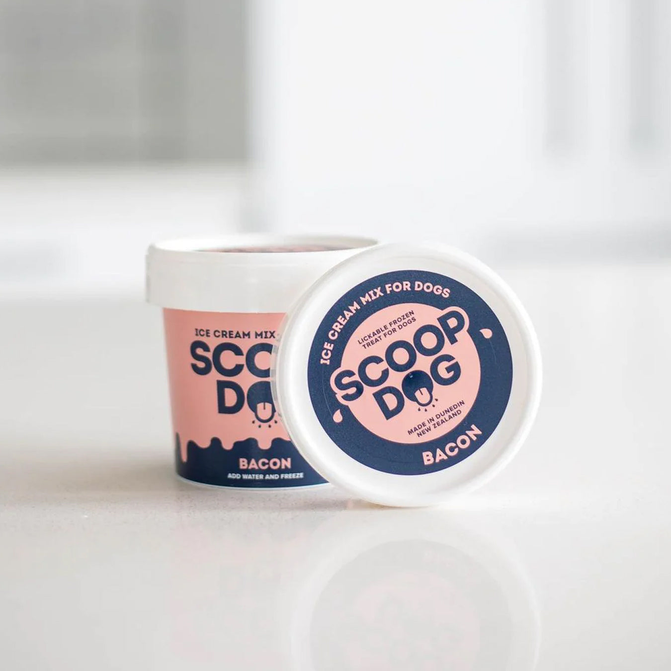 Two containers of "Scoop Dog" bacon-flavored ice cream mix for dogs on a white surface.