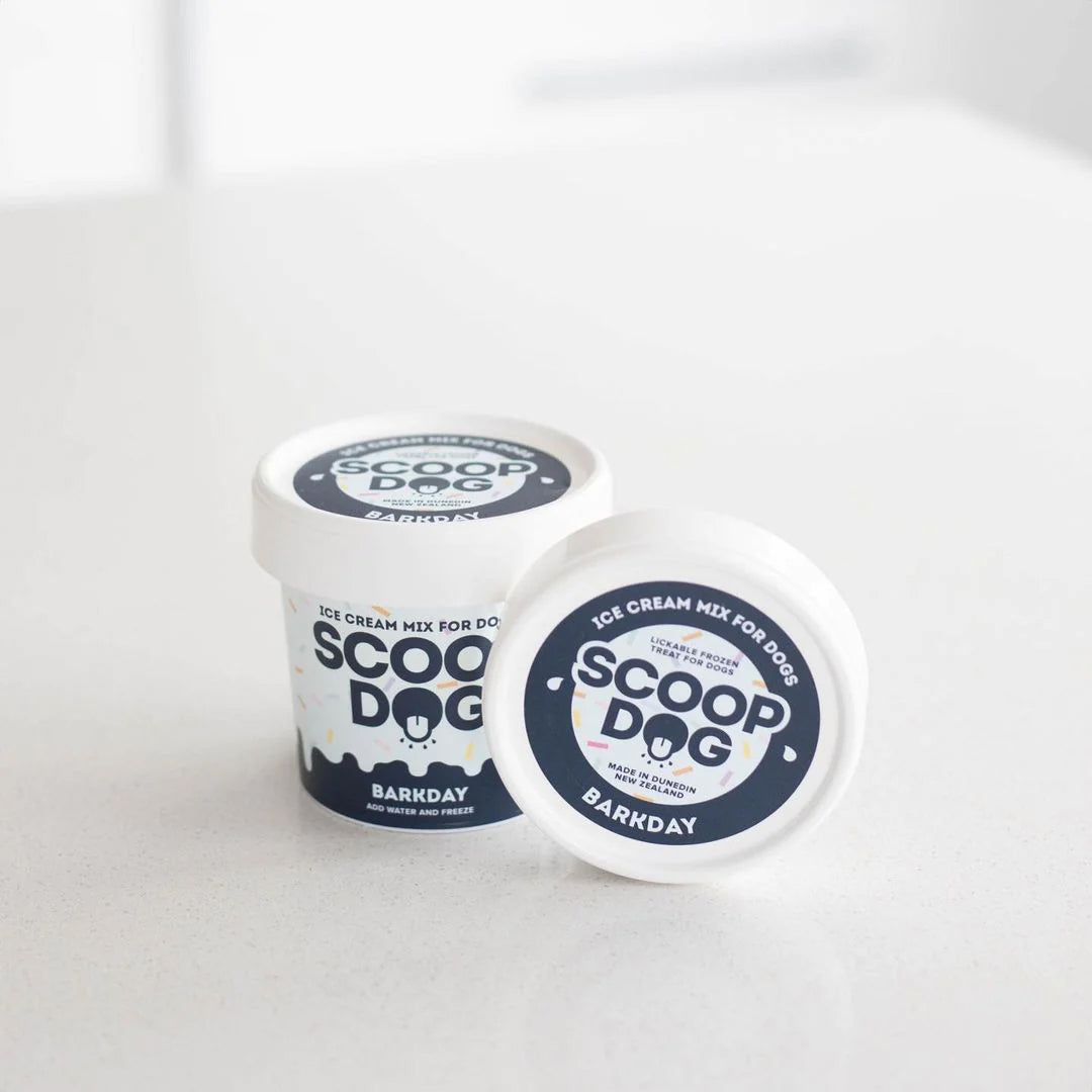 Two containers of "Scoop Dogg" ice cream mix for dogs labeled "Barkday" on a white surface.