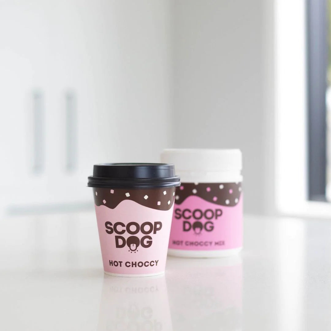 A takeout coffee cup and container labeled "SCOOP DOG HOT CHOCCY" on a kitchen counter.