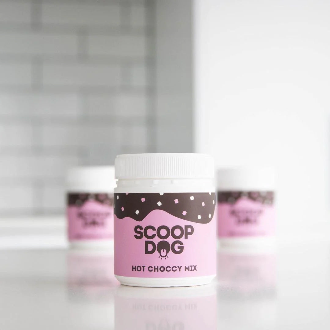 Jar labeled "SCOOP DOG HOT CHOCCY MIX" on a reflective surface with similar blurred jars in the background.