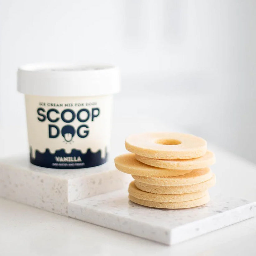 A stack of dog treats beside a container labeled "SCOOP DOG Vanilla Ice Cream Mix for Dogs."