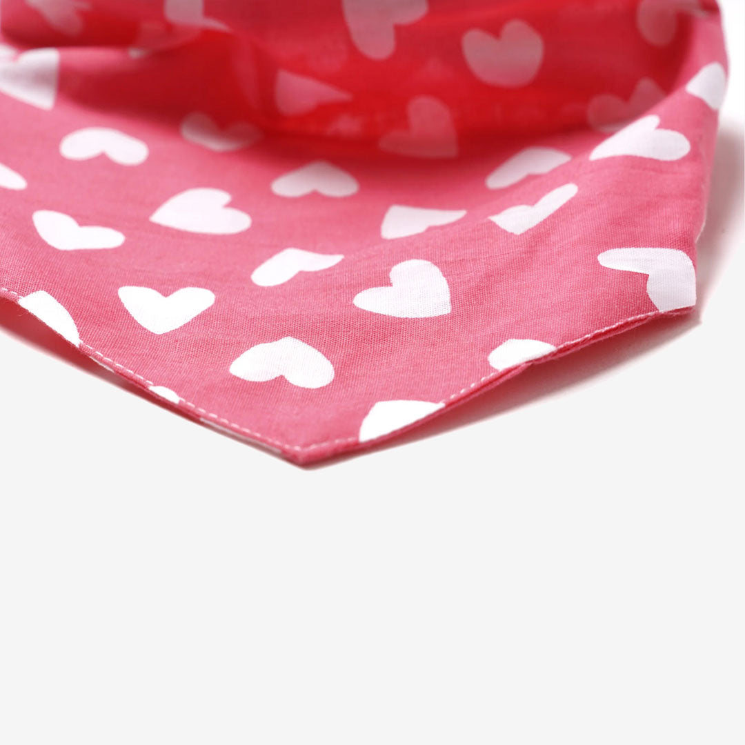 Close-up of a pink bandana featuring scattered white heart patterns and a pointed tip, set against a light background.