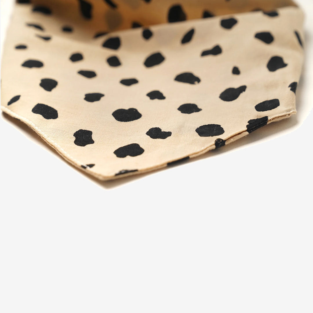Fabric with a black irregular dotted pattern on a beige background, resembling animal print, on a white background.