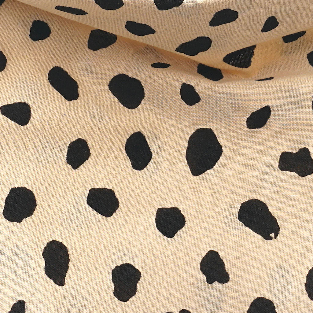 Fabric with a black irregular dotted pattern on a beige background, resembling animal print.