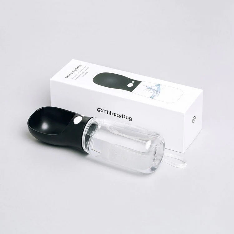 A ThirstyDog portable water bottle for dogs, featuring a black scoop and clear water reservoir, beside its white packaging.