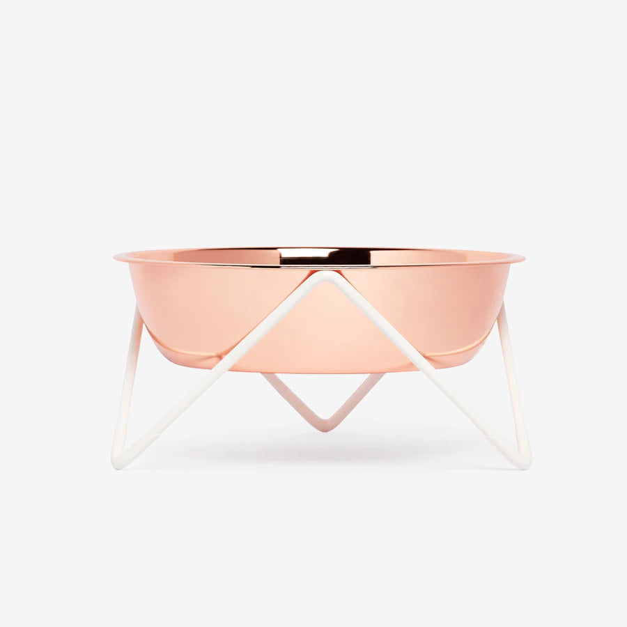 A modern, rose gold bowl on a minimalist white metal stand, showcasing a sleek and stylish design.