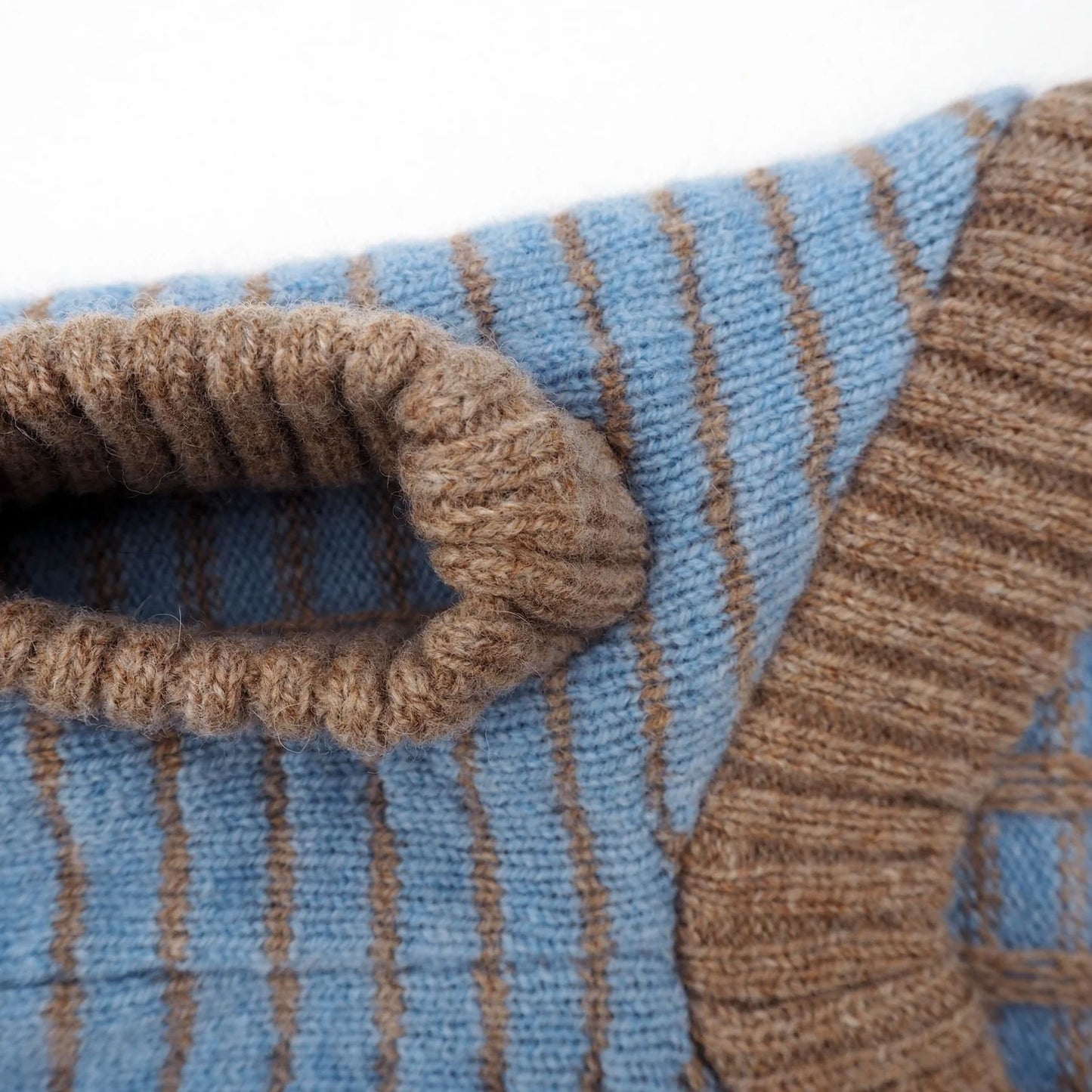 Close-up of a knitted sweater featuring blue and brown stripes, highlighting the cozy neck detail and soft texture.