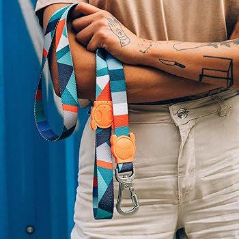 A person holding a colourful striped camera strap with an orange attachment.