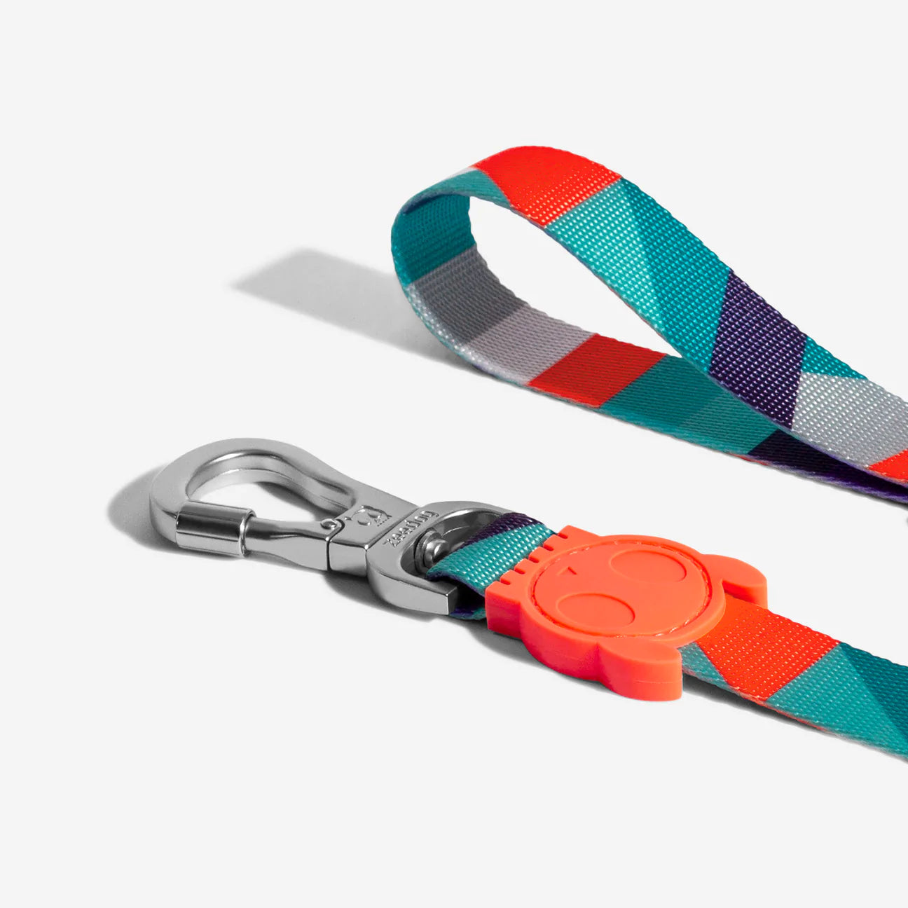 Colourful dog leash featuring a clip and an orange rubber charm with a smiling face.