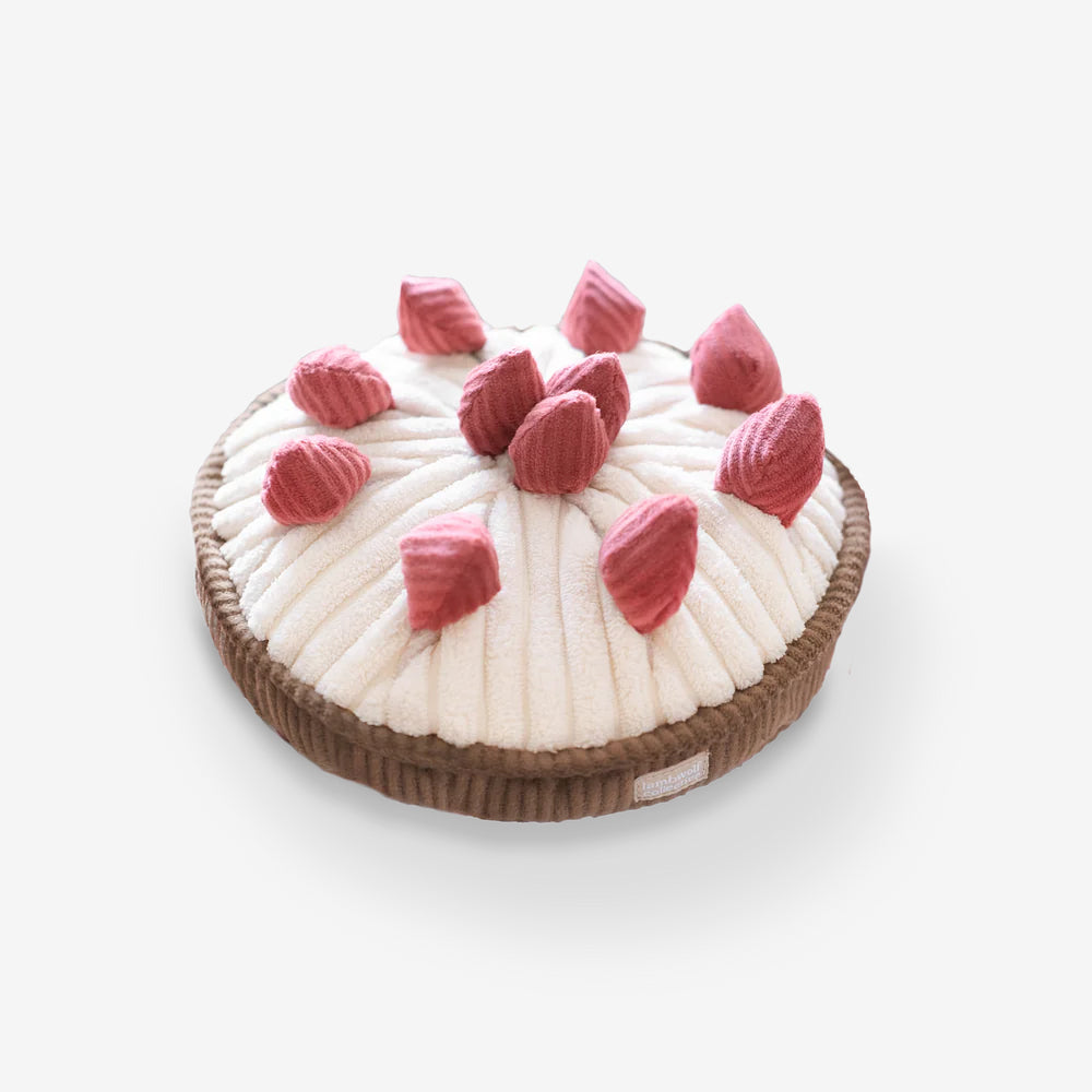 A cream plush berry pie, dog toy. With eleven rose coloured berries on a cream fabric and brown base.