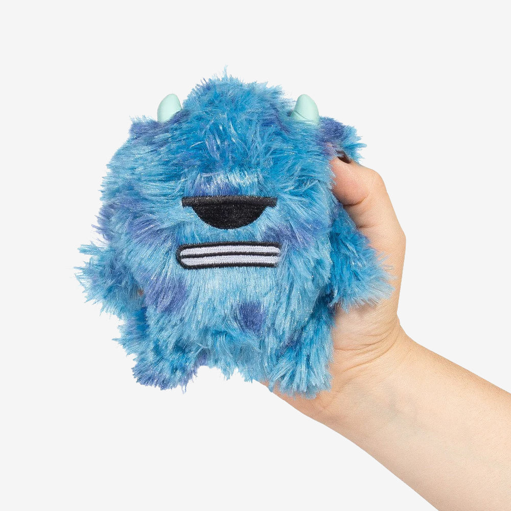 A hand holding a blue fluffy monster dog toy with horns and a sleepy expression.