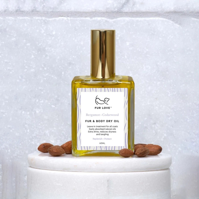 Bottle of FUR LOVE fur & body dry oil on a pedestal with almonds, against a textured backdrop.