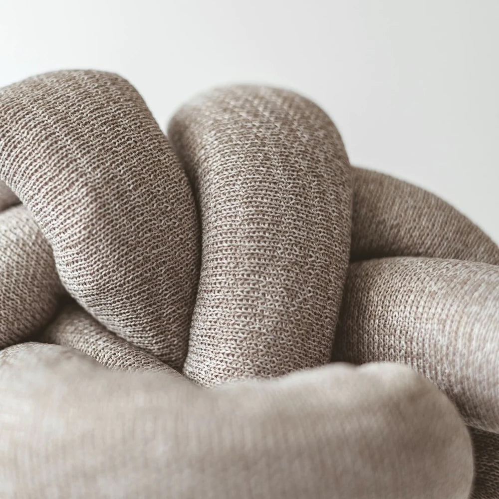 Close-up of a soft, textured beige fabric intertwined in a knot, showcasing its cozy and tactile design.