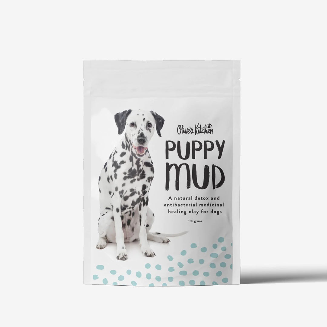 A spotted puppy sits beside a package labeled "PUPPY MUD," a healing clay for dogs.