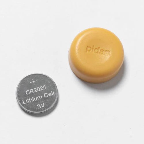 A CR2025 lithium cell battery beside a small round yellow casing with "pidan" text.