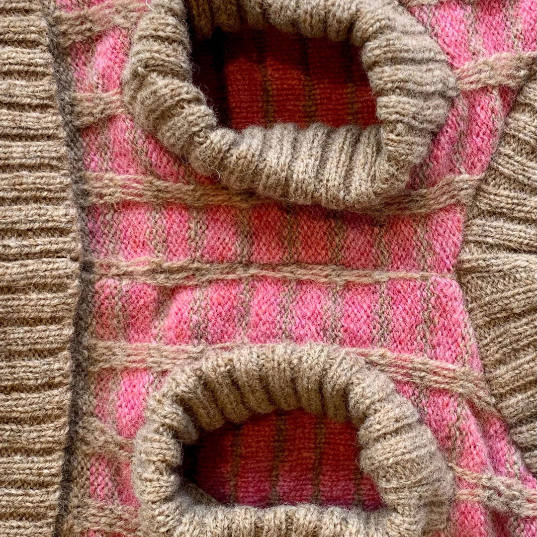 Close-up of a textured knit fabric featuring pink and beige patterns with circular openings, showcasing intricate craftsmanship.