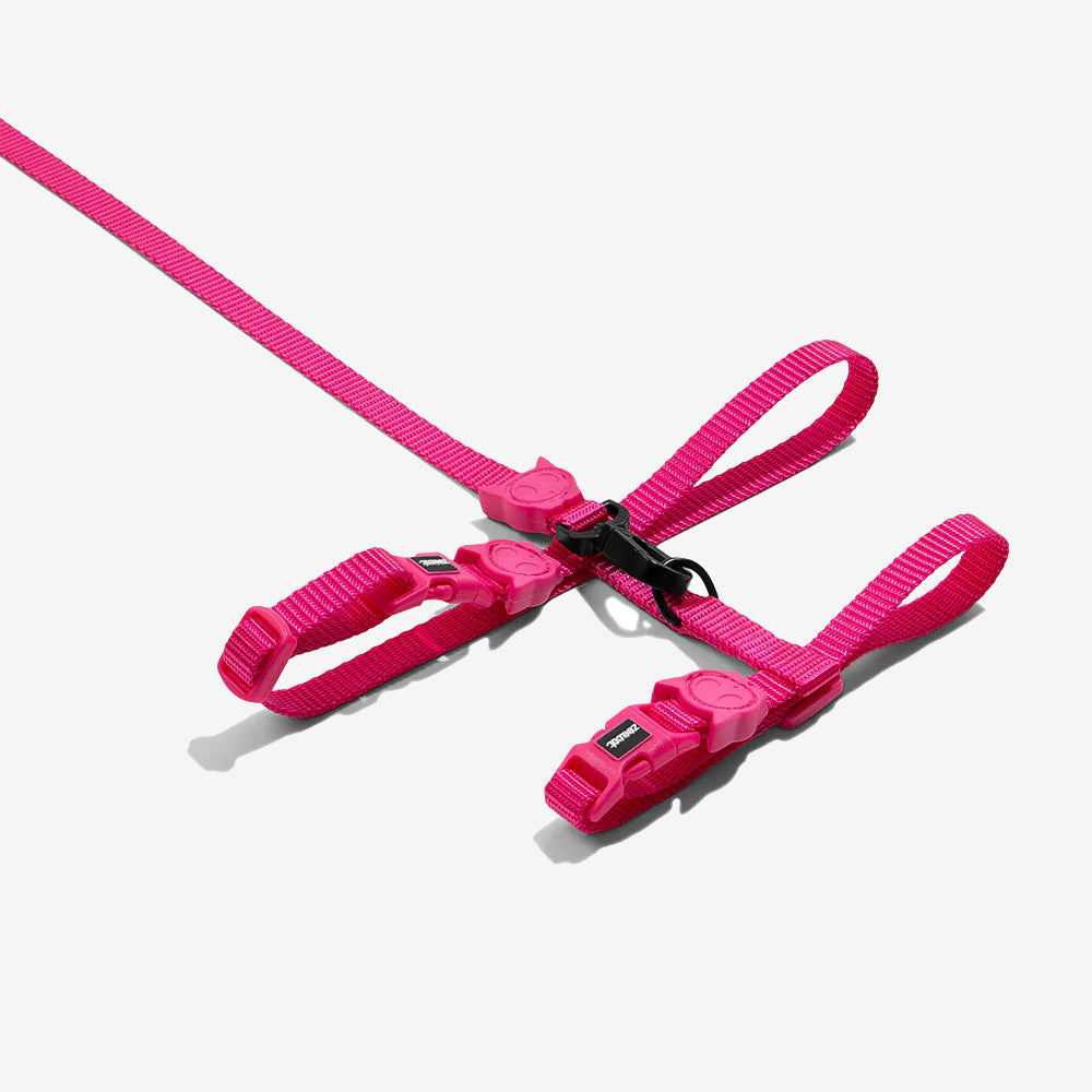 Pink pet harness with pink buckles and cat and cat rubber motifs isolated on a white background.