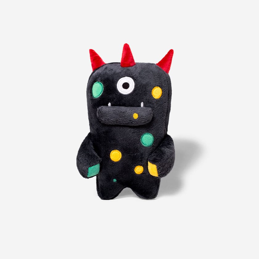 A navy blue plush alien toy with red horns, one eye, and colourful spots on a white background.