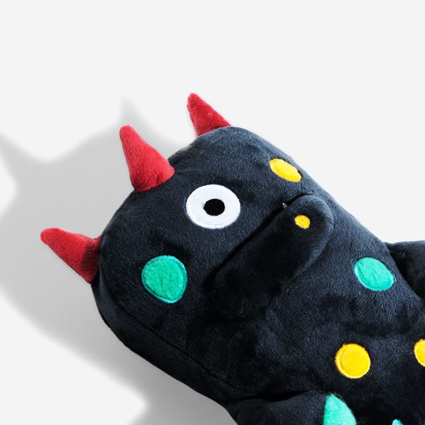 A navy blue plush alien toy with red horns, one eye, and colourful spots on a white background.