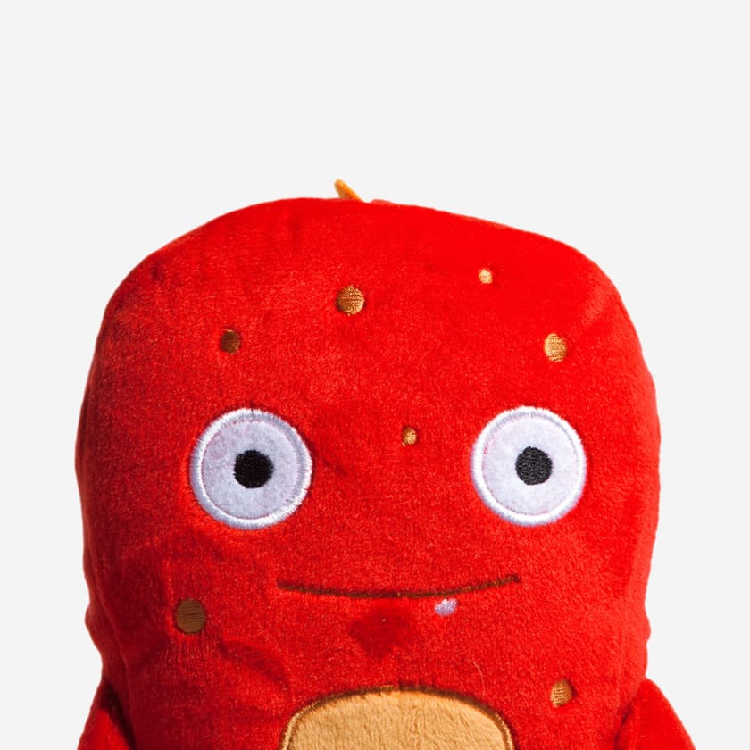 Red plush alien toy with cute eyes and a orange chest and spots on a white background.