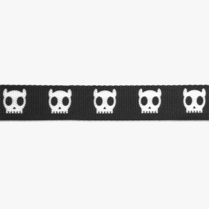 Close up detail of a cat harness fabric in black with a pattern of four white skull icons.