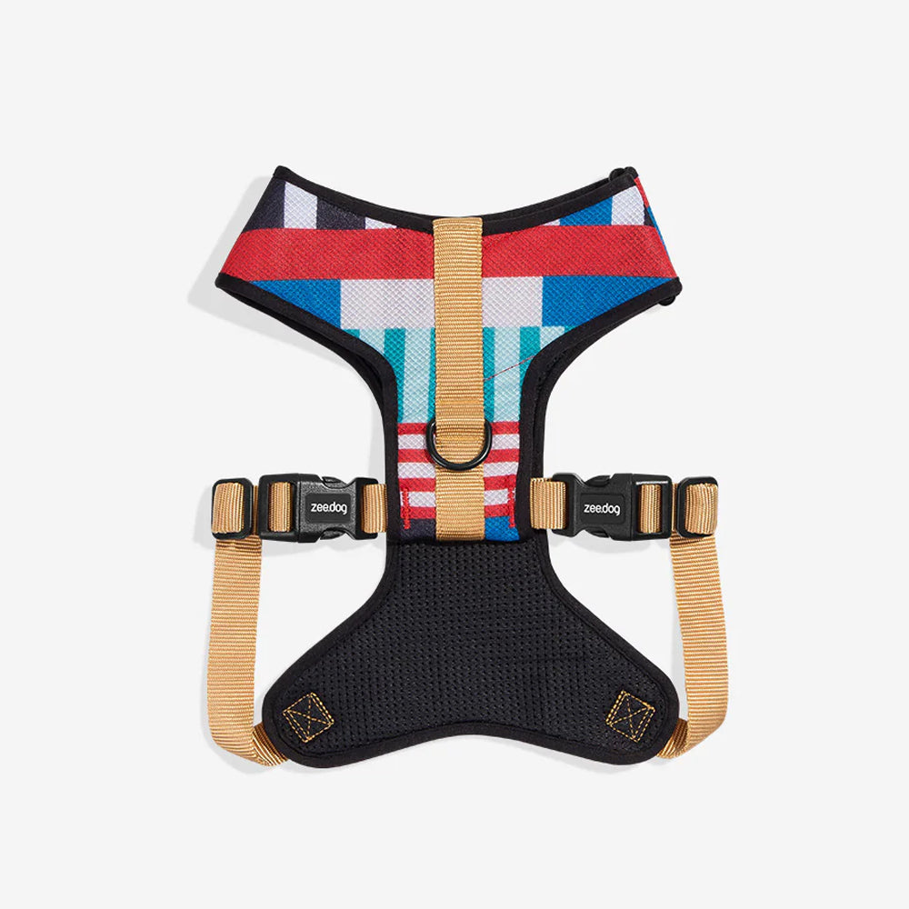A multicoloured dog harness with adjustable tan straps on a white background.