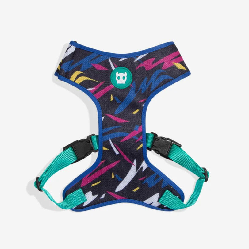 Colourful dog harness featuring a vibrant pattern of blue, pink, and yellow shapes, with teal straps and a green logo patch.