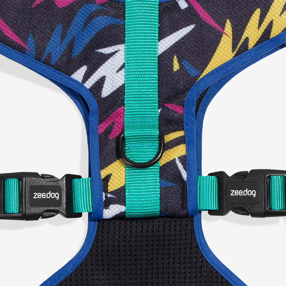 Close-up of a colourful dog harness featuring a geometric pattern, adjustable straps, and buckles labeled "zee.dog."