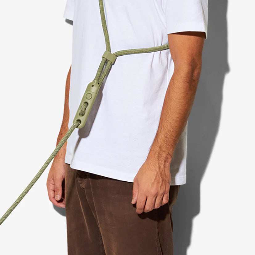 A person wearing a white t-shirt is holding a green, adjustable harness with a clip, styled for comfort and utility.