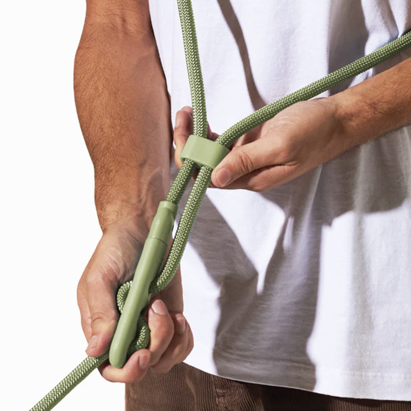 A person adjusts a green climbing rope using a smooth device, showcasing a focus on outdoor gear and safety techniques.