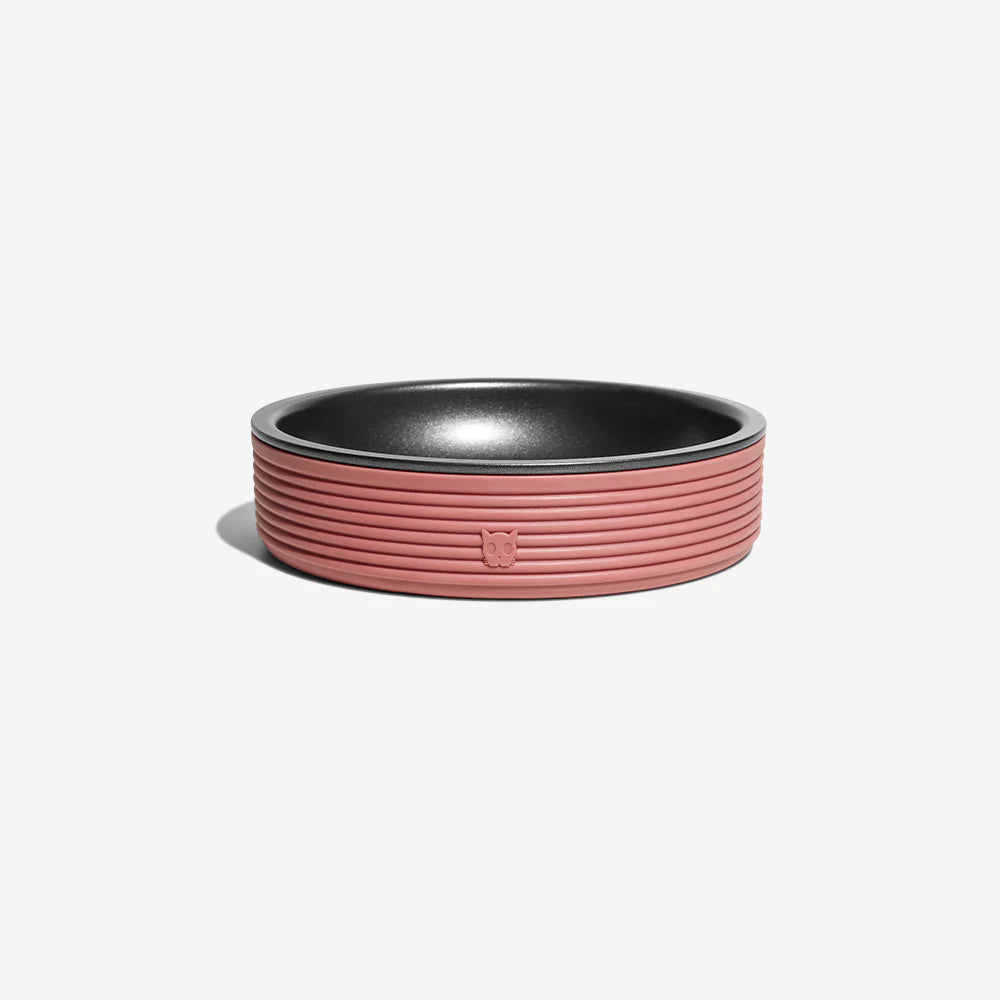 A stylish pet food bowl in pink and with a removeable black aluminum inner, resting on a white background.