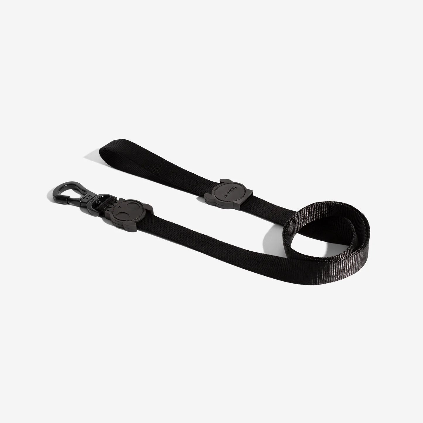 A black dog leash featuring a clip and a circular buckle with a playful skull design, coiled neatly for storage.