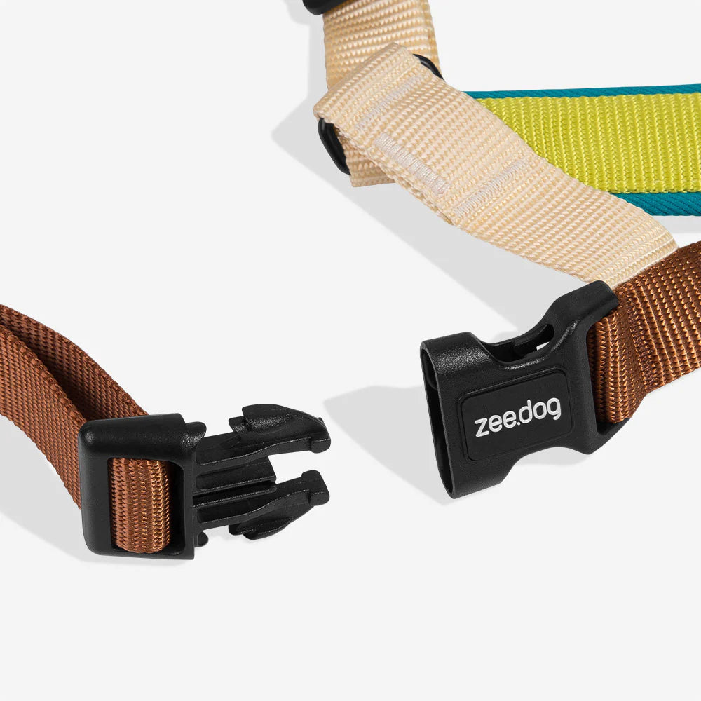 Unbuckled dog harness black clip with brown, beige, and green straps on a white background.