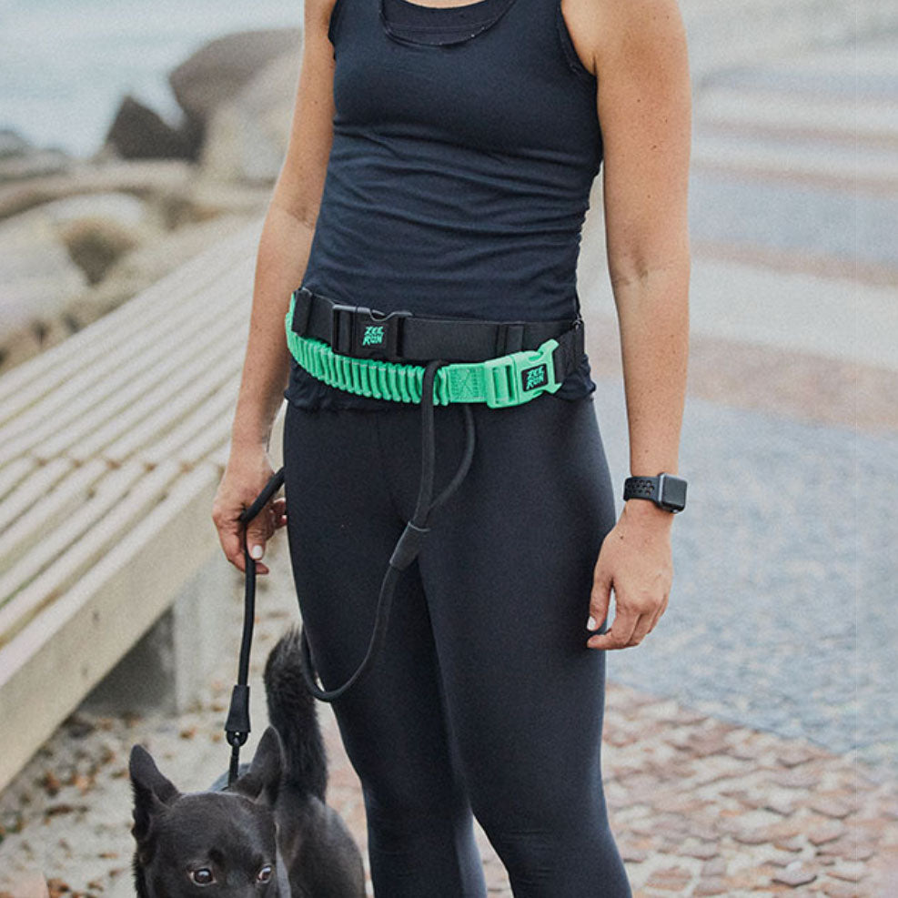 A person wearing a running belt and holding a dog leash with a black dog beside them.