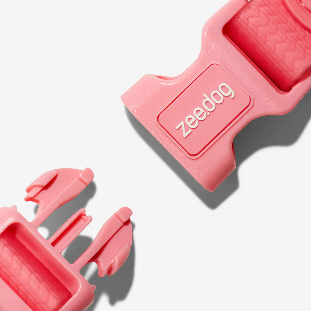 Close-up of a pink dog collar buckle featuring the brand name "zee.dog." on a textured surface, highlighting its vibrant color and design.
