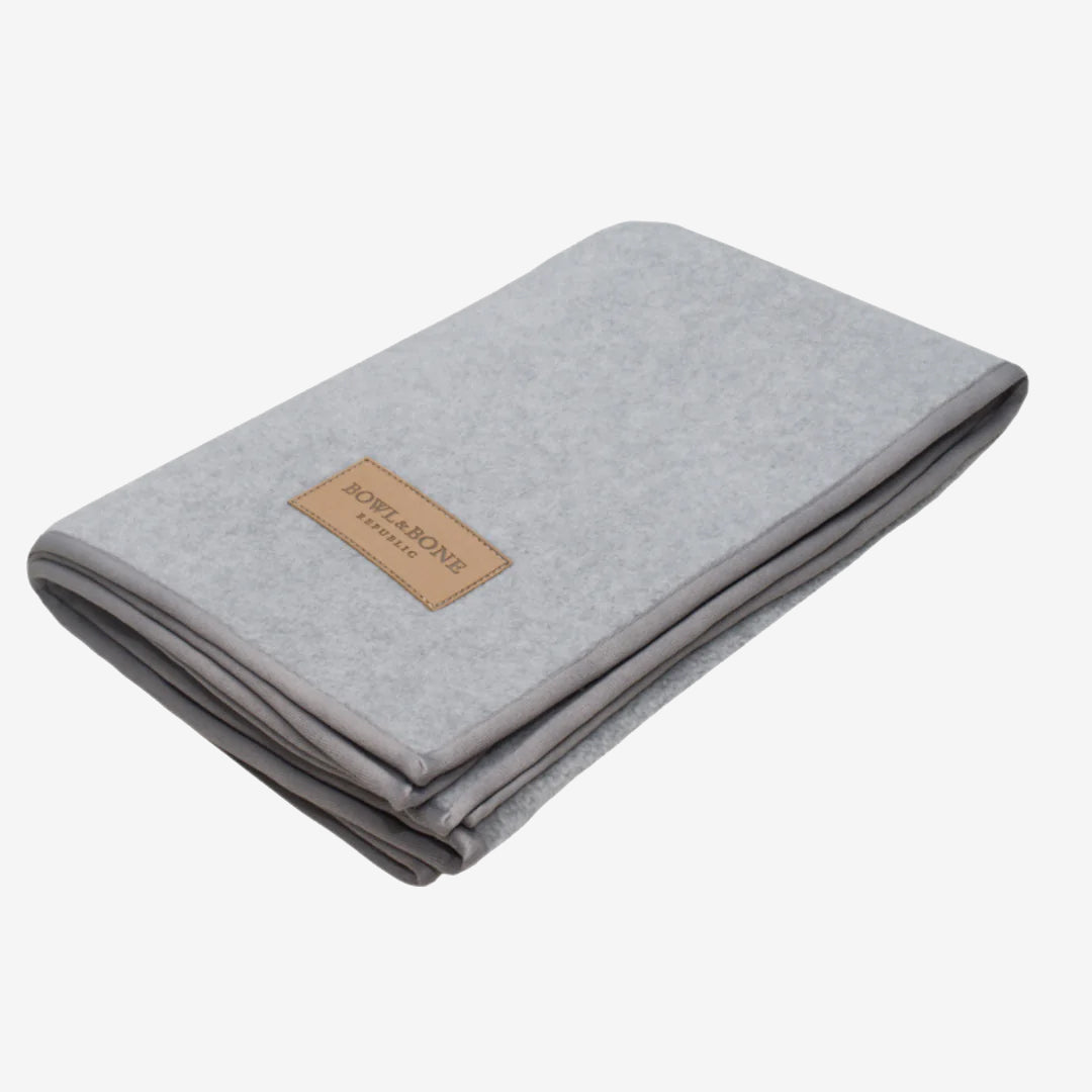 Grey folded fleece blanket with a brown brand label on white background.